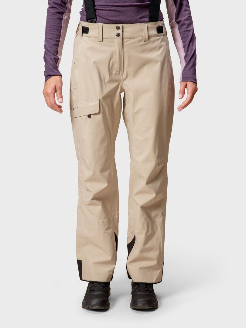 Personen är klädd i beige Halti Settler 3L DrymaxX Skidbyxor Dam med svarta hängslen, lila skjorta och svarta stövlar.