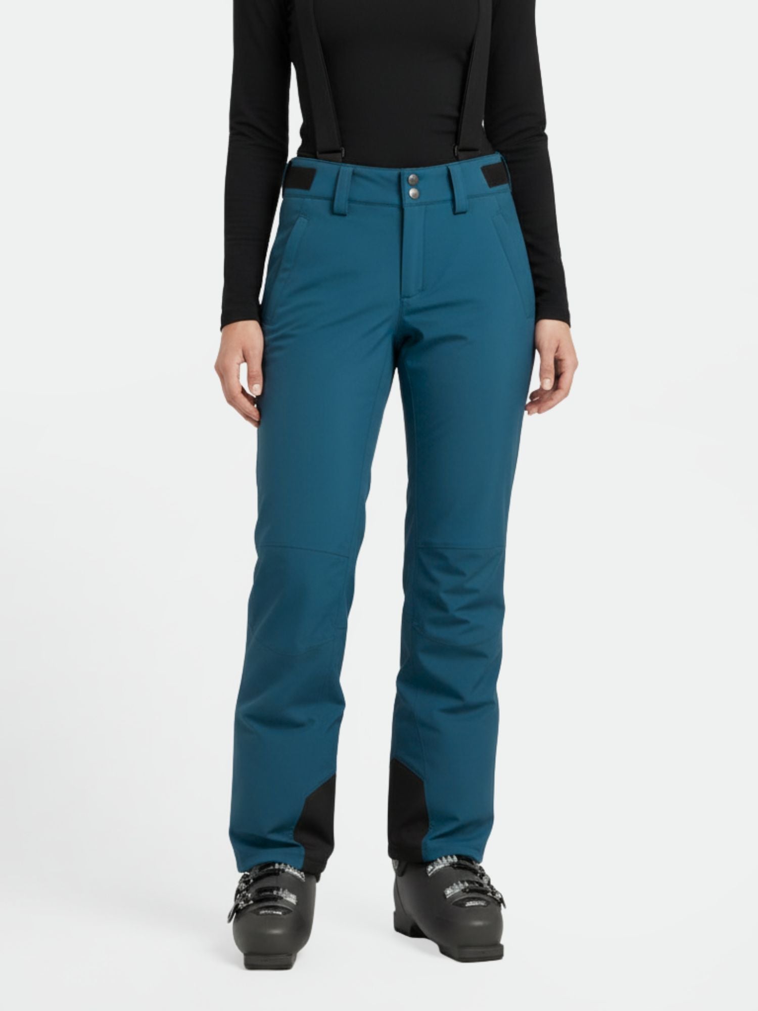 En person bär Halti Trusty DrymaxX Skidbyxor Dam i teal med svarta hängslen, svart topp och pjäxor på vit botten.