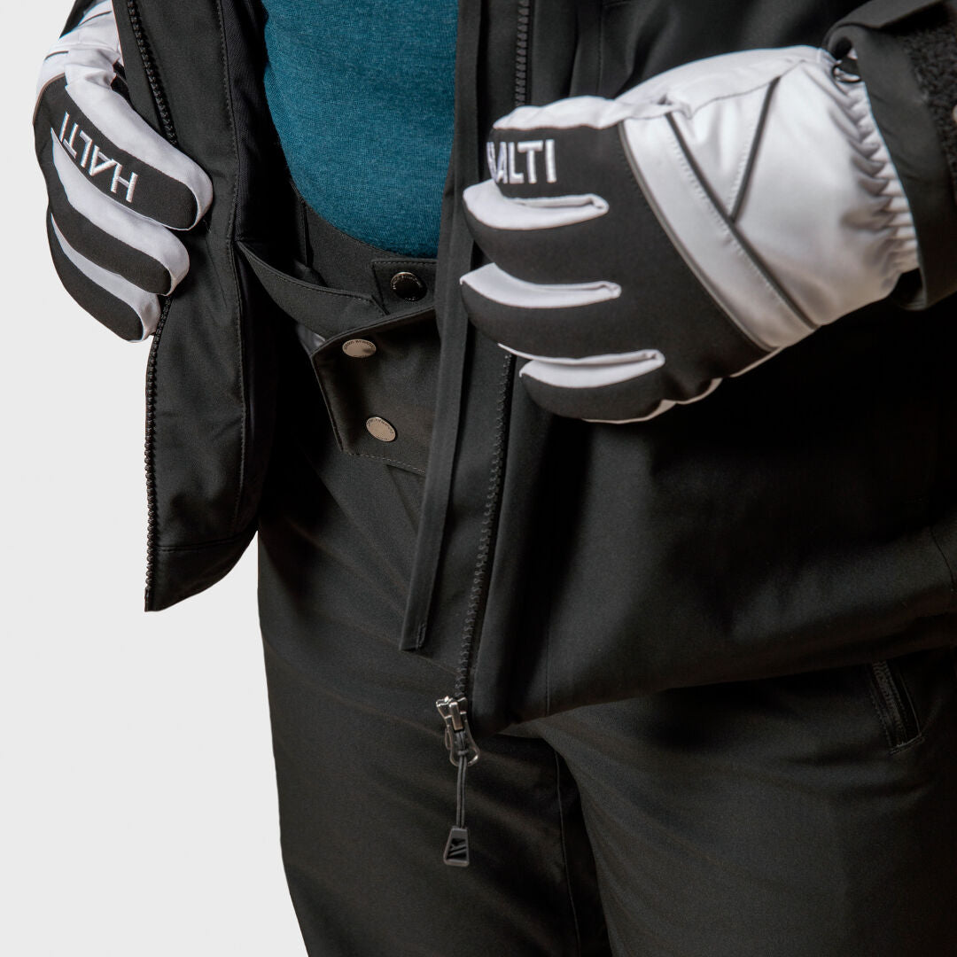 En person i svart Halti Vertica DX Skidjacka Herr öppnar dragkedjan och visar en blå skjorta under svarta vinterhandskar.