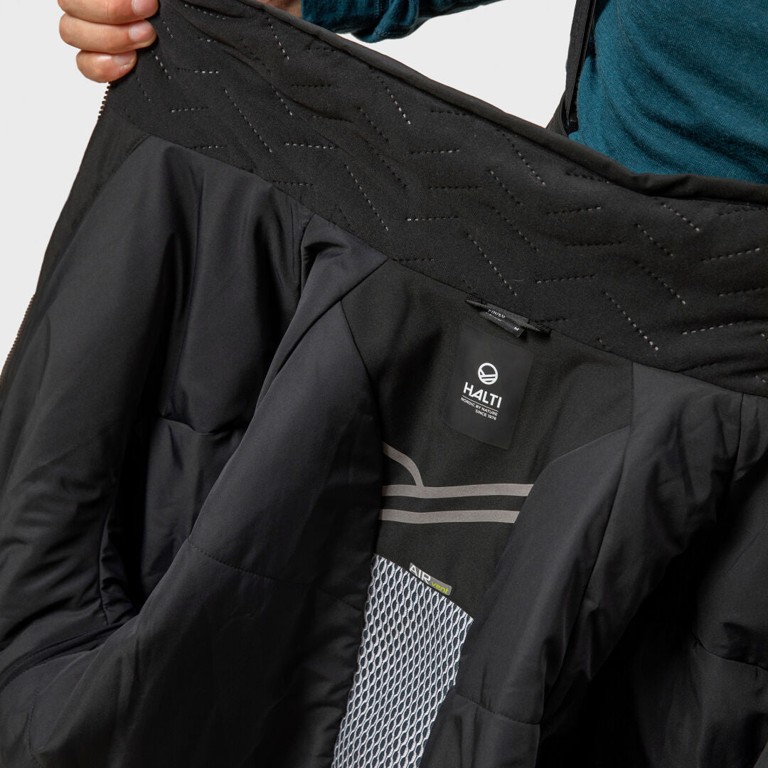 En person håller upp en svart Halti Vertica DX Skidjacka Herr och visar innerfodret och märkesetiketten.