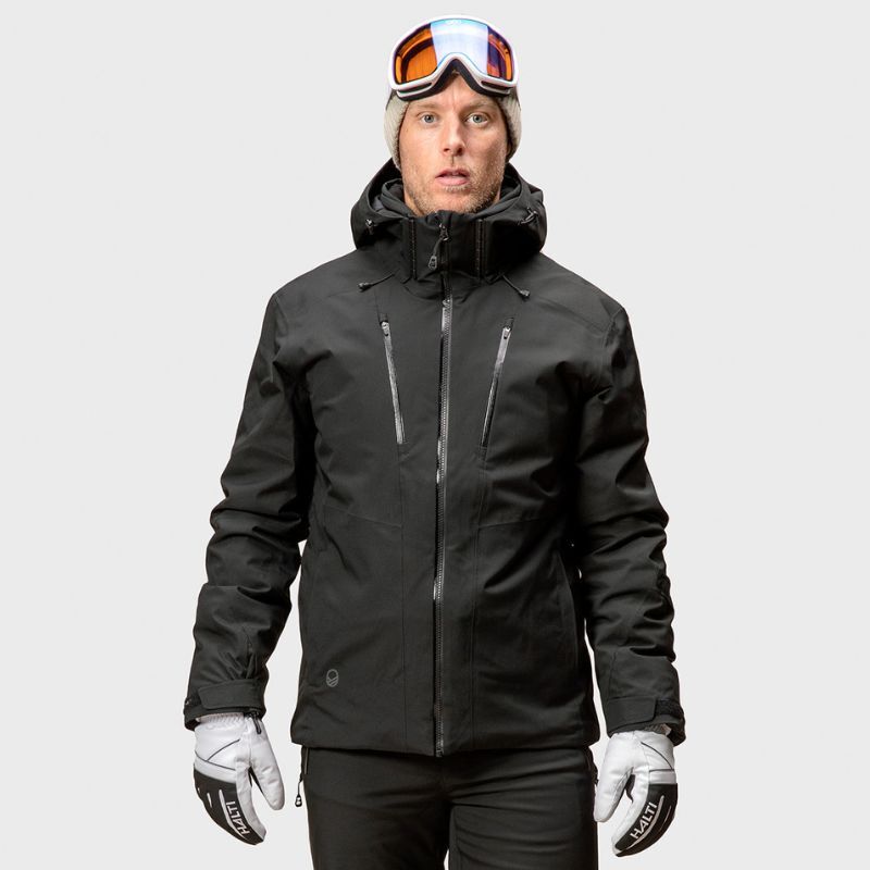 En person bär en Halti Vertica DX Skidjacka Herr, grå mössa och skidglasögon mot en enfärgad bakgrund.