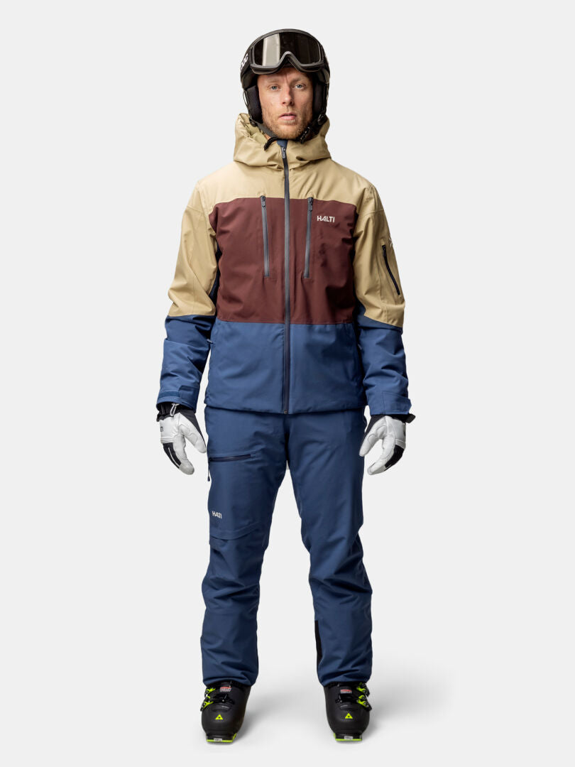 En man bär Halti Melvik DX Skidjacka Herr med Microtherm Dynamic-isolering och står mot en enfärgad bakgrund.