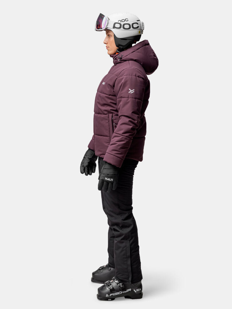 Modellen bär Halti Ascale Puffer Skidjacka Dam, hjälm, handskar och stövlar i profil mot en vit bakgrund.