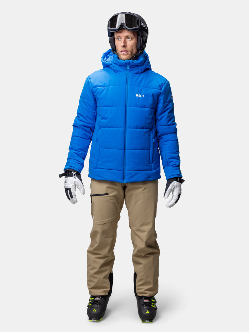 En person i blå Halti Ascale Puffer Skidjacka herr, beige byxor och skidhjälm står vänd framåt.