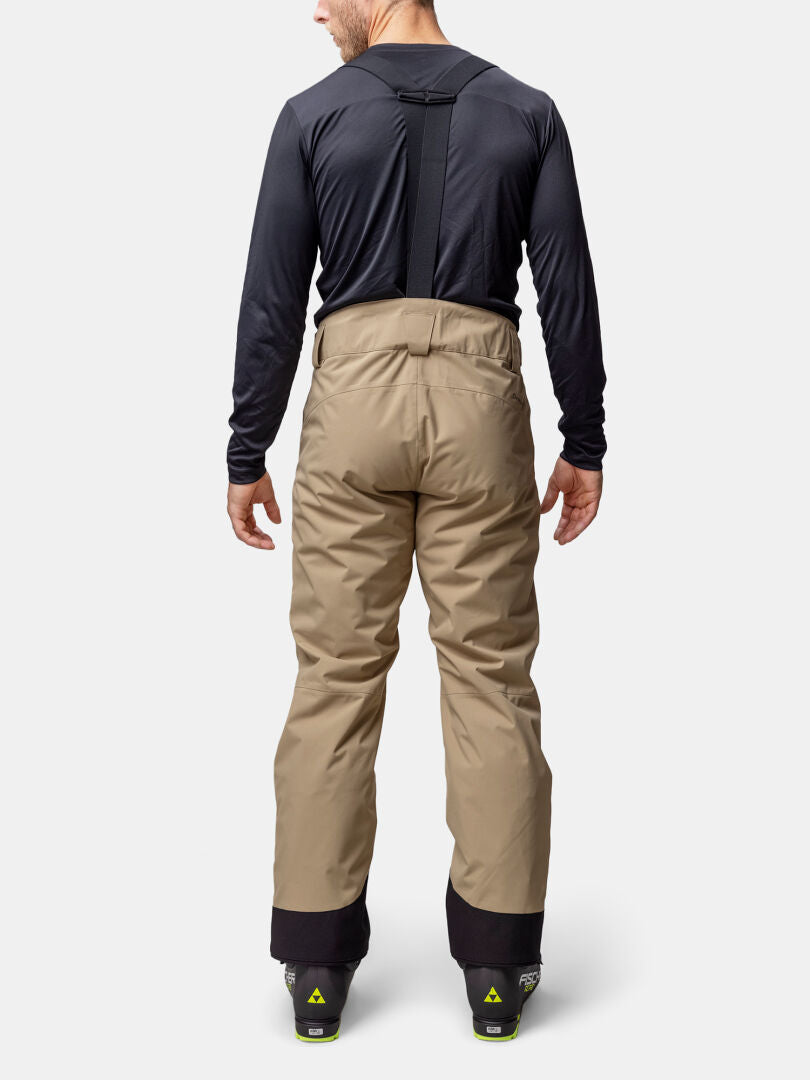 En person i Halti Carvey II DX Skidbyxor Herr med DrymaxX, svart långärmad skjorta och pjäxor, sedd bakifrån.