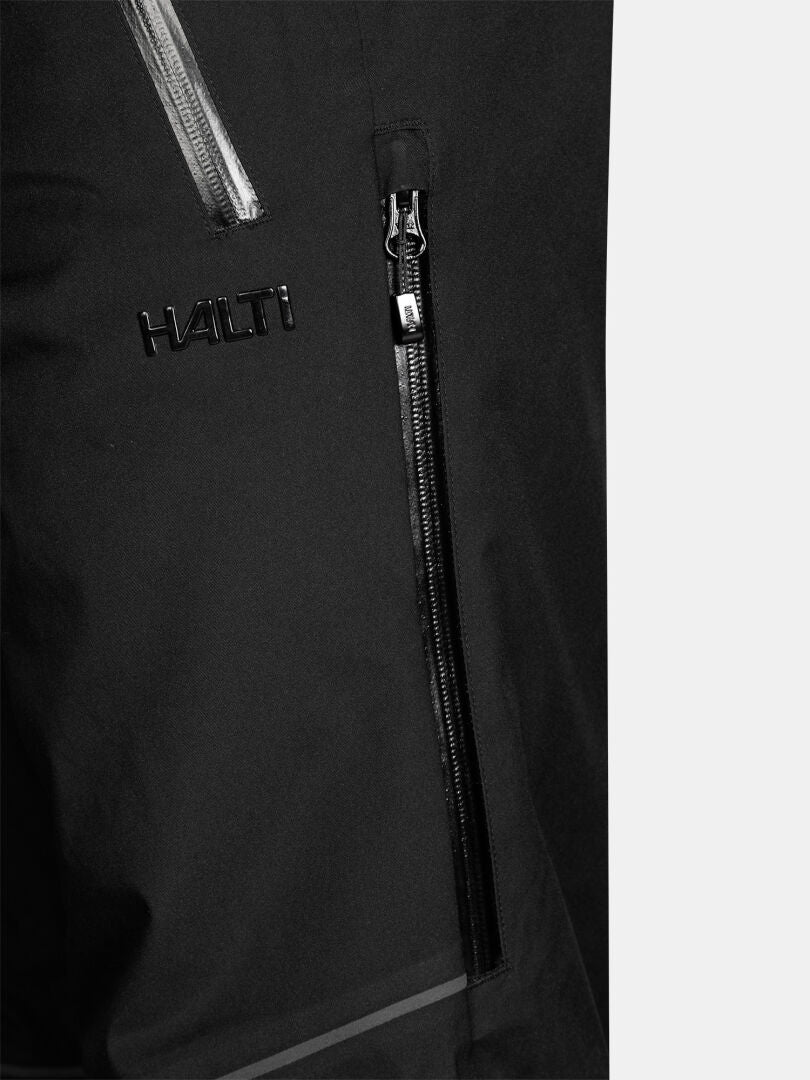 Närbild på svarta, vattentäta Halti Vertica II DX Skidbyxor för herrar med en ficka med dragkedja och präglat varumärke.