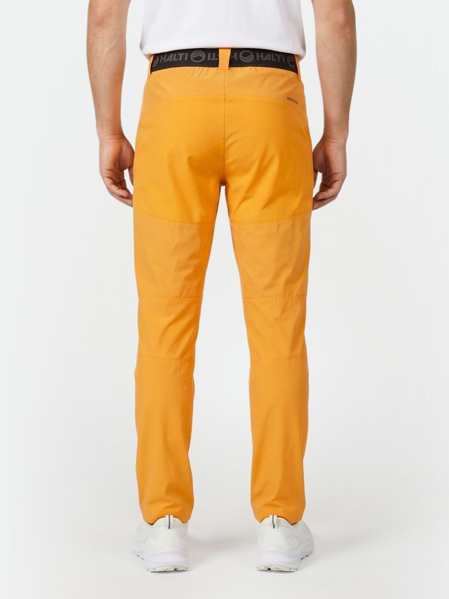 En person klädd i Halti Pallas Herr X-stretch Lite Byxor, vit skjorta och sneakers, bakifrån mot en vit bakgrund.