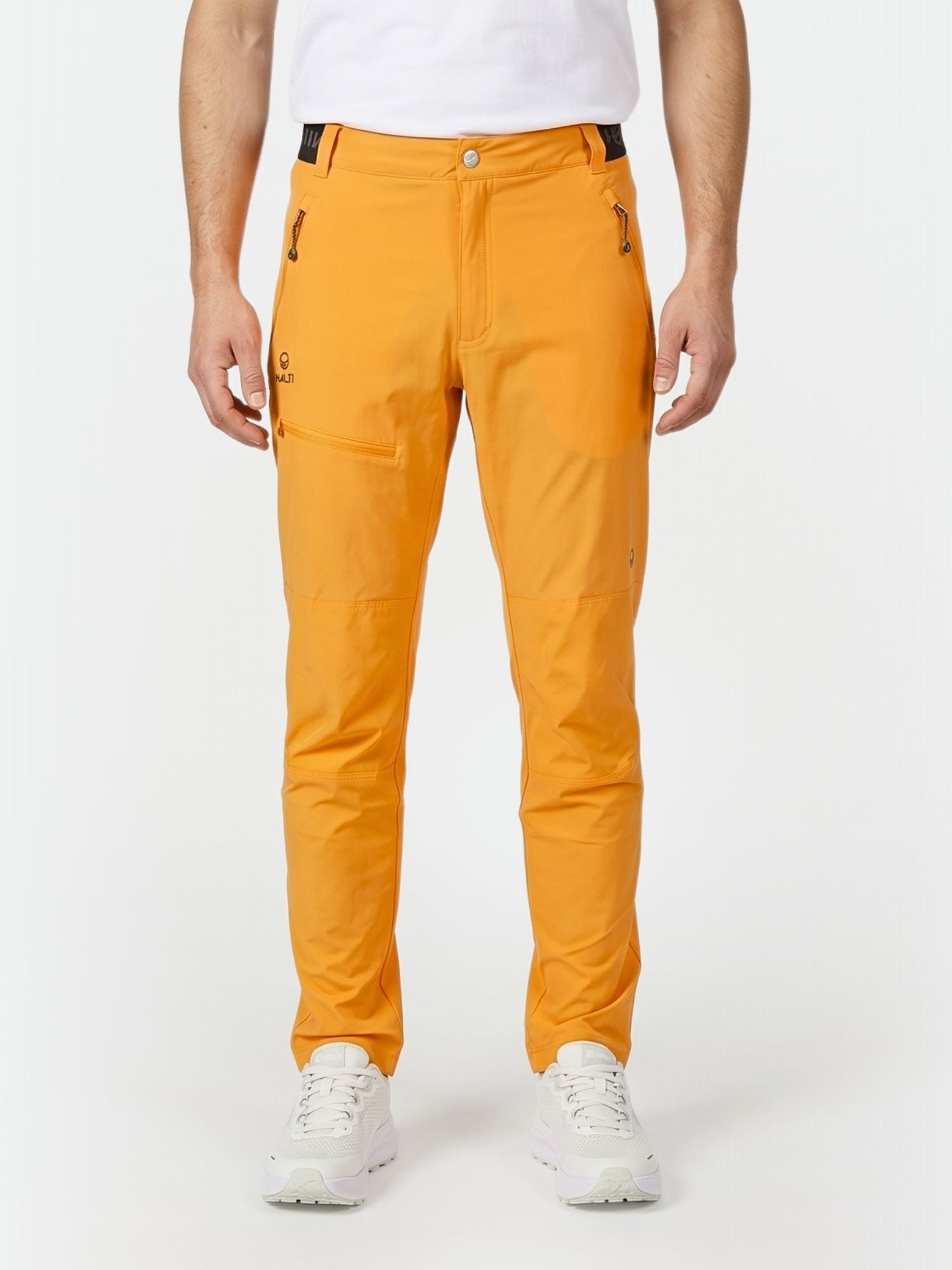 En person i ljus Halti Pallas Herr X-stretch Lite Byxor, vit skjorta och sneakers, redo för vandring mot en vit bakgrund.