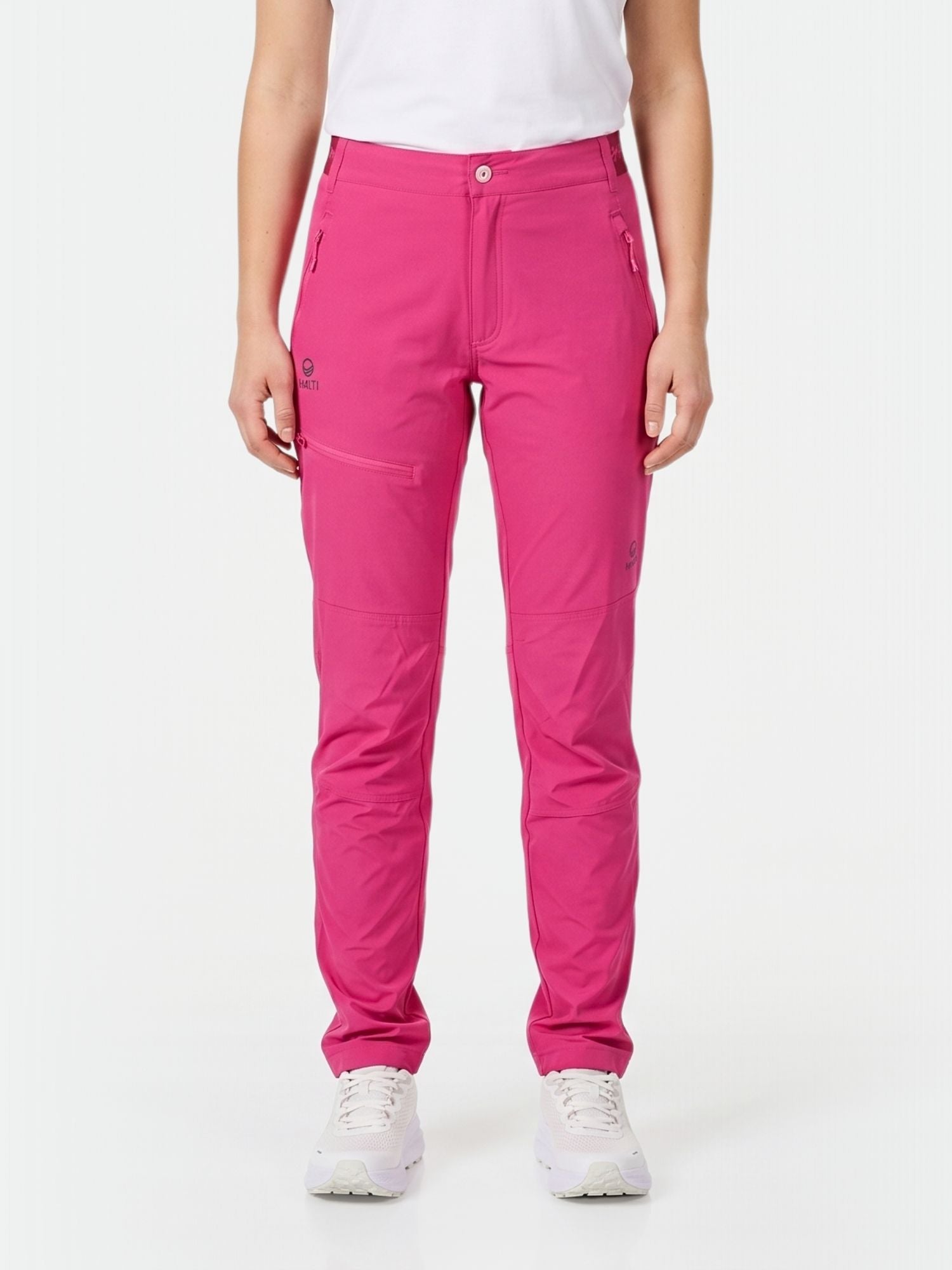En person i Halti Pallas Dam X-stretch Lite Byxor, vit t-shirt och sneakers står mot en enfärgad bakgrund.