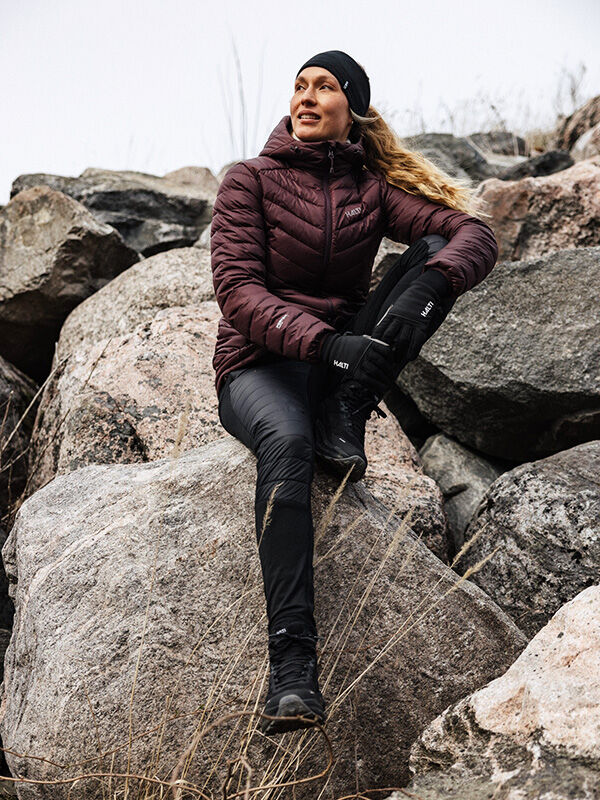 En person i Halti Veidnes Lättvaddrade Byxor Dam sitter på en klippa bland stenblock, tittar åt sidan och ler.