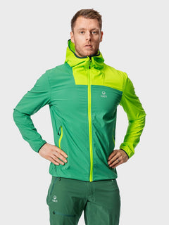 En man bär en grön Halti Pallas Herr Lite X-stretch Jacka och gröna byxor och står med händerna på höfterna mot en enfärgad bakgrund.