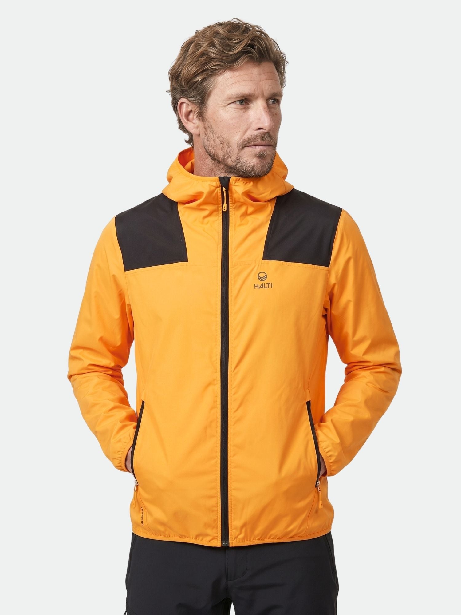 Man iförd Halti Pallas Herr Lite X-stretch Jacka med svarta detaljer, händerna i fickorna, tittar åt sidan.