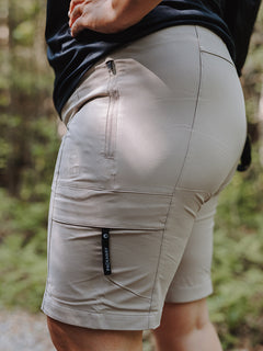 Närbild på en person som bär Halti Reissu Plus Dam Stretch Shorts med dragkedjefickor, stående på en skogsstig.