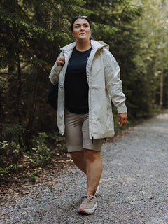 En person i lätt jacka, svart skjorta och Halti Reissu Plus Dam Stretch Shorts går på en skogsklädd grusväg.