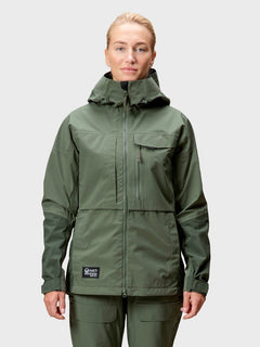 En person i grön Halti Hiker DrymaxX 3L Ventilated Jacka Dam och matchande byxor står mot en ljus bakgrund.