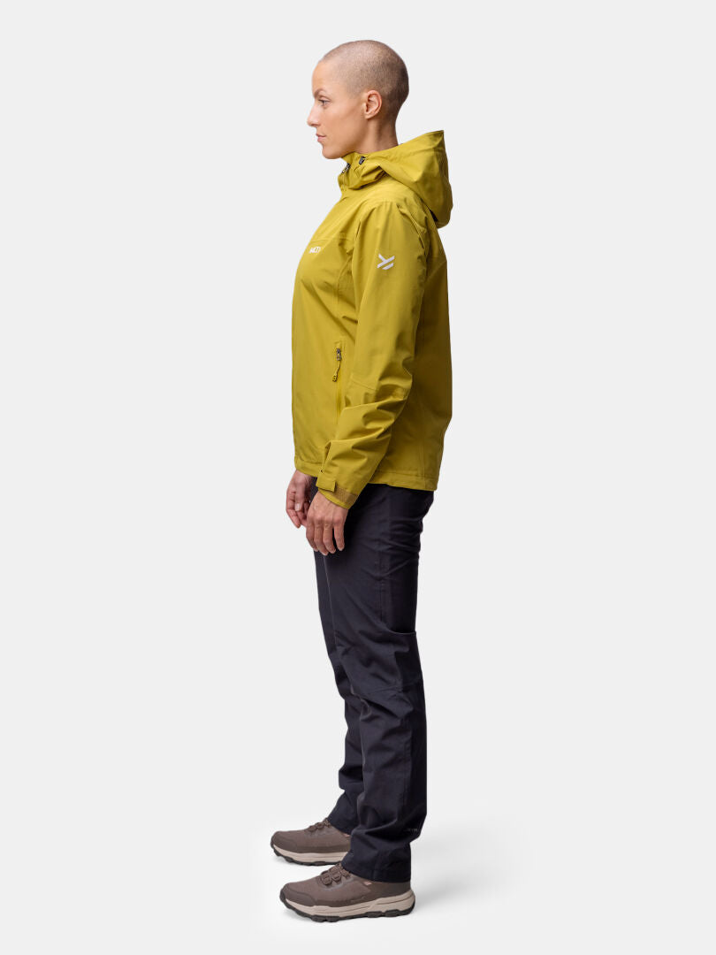 Personen i profil bär Halti Forter DX Skaljacka Dam i gult, svarta byxor och bruna skor - perfekt för friluftsliv.
