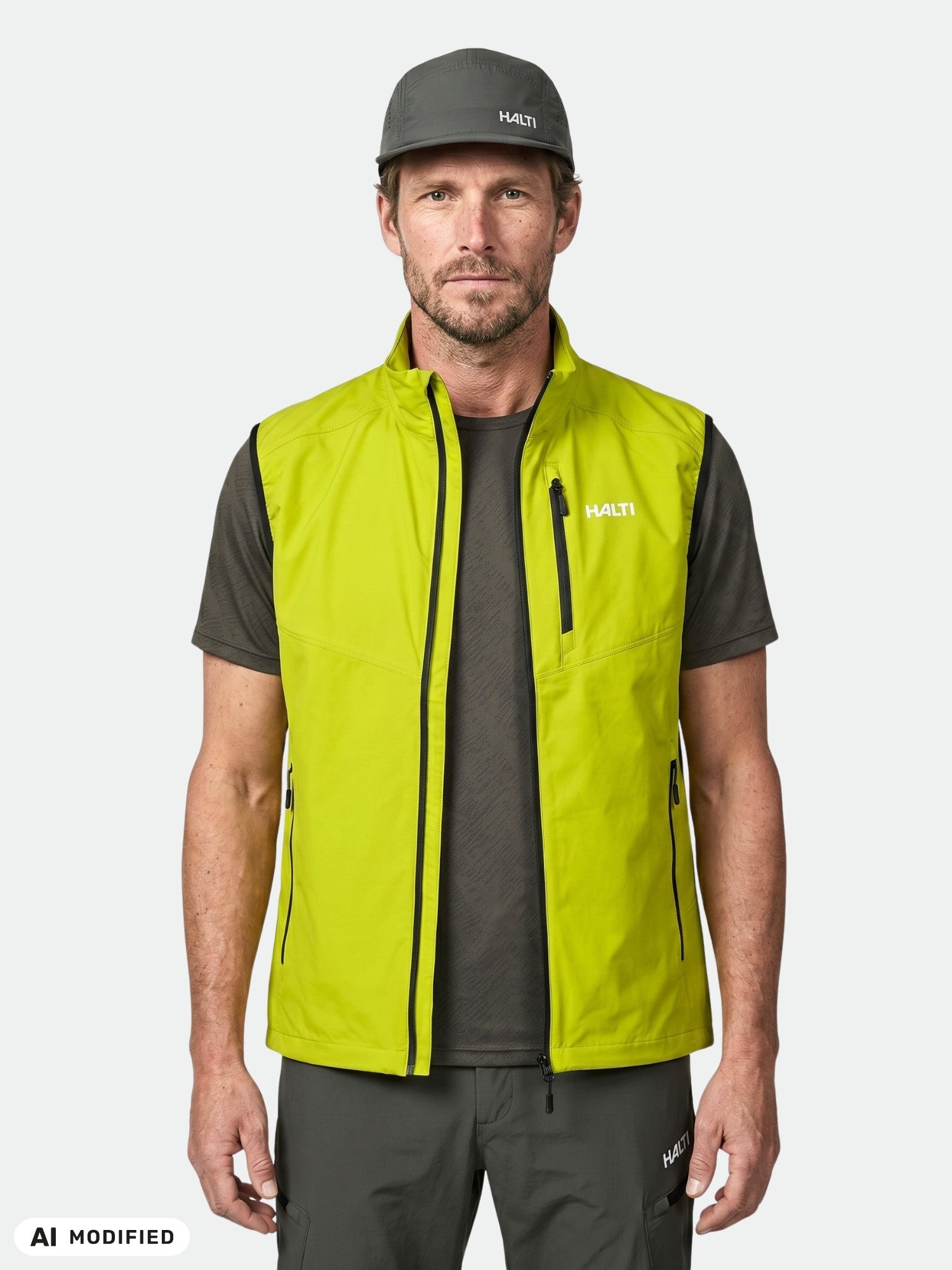 En man bär en Halti Pallas Evo X-stretch Väst Herr i limegrönt, tillsammans med en mörk skjorta och byxor, mot en vit bakgrund.