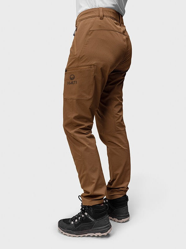 En person bär Halti Pallas Evo Brushed X-stretch Byxor Dam med sidoficka och svarta vandringskängor mot en ljus bakgrund.