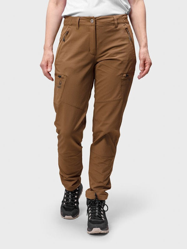 En person i Halti Pallas Evo Brushed X-stretch Byxor Dam och svarta utomhusskor står mot en enfärgad bakgrund.