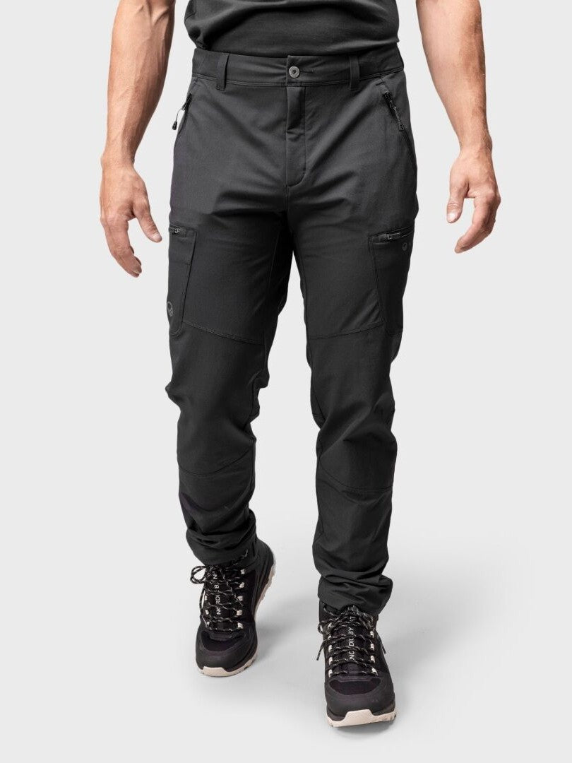 En person i svart Halti Pallas Evo Brushed X-stretch Byxor Herr och vandringskängor står mot en ljusgrå bakgrund.