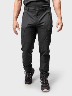En person i svart Halti Pallas Evo Brushed X-stretch Byxor Herr och vandringskängor står mot en ljusgrå bakgrund.