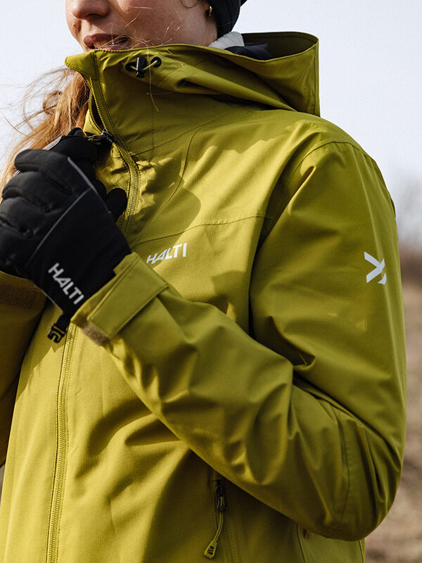 Person iklädd Halti Forter DX Warm Skaljacka Dam i olivgrönt och svarta Halti-handskar, utomhus.