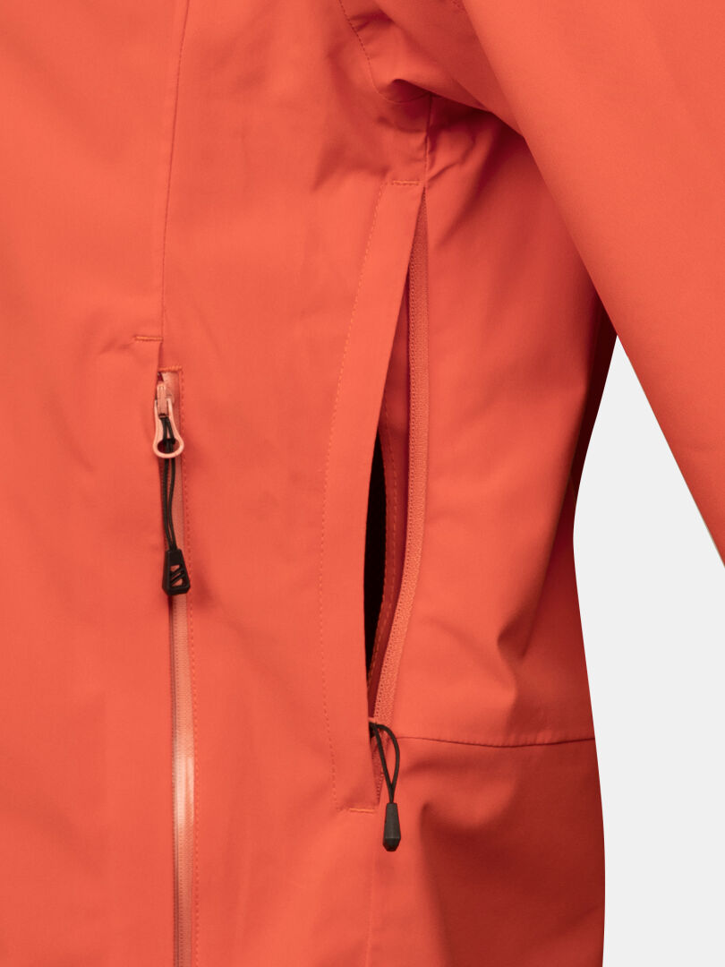 Närbild av Halti Staala DX Skaljacka Dam i orange, som visar en vertikal blixtlåsficka och en del av blixtlåset på framsidan.