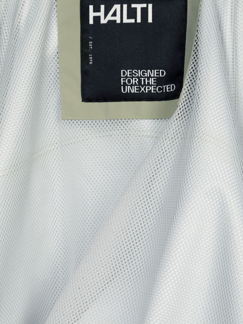 Närbild på en Staala DX Skaljacka Dam-etikett med texten ”HALTI DESIGNED FOR THE UNEXPECTED” på vitt, strukturerat tyg.