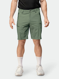 En person bär Halti Pallas Cool X-stretch Shorts Herr (salviagrön, UPF 90+), svart skjorta, vita strumpor och sneakers.