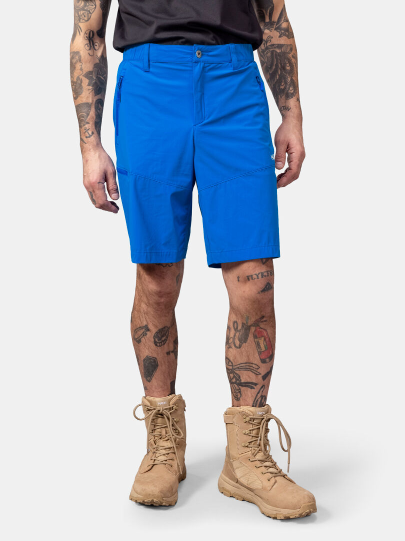 Man klädd i Halti Pallas Cool X-stretch Shorts, solbruna stövlar, svart skjorta; tatueringar synliga på armar och ben.