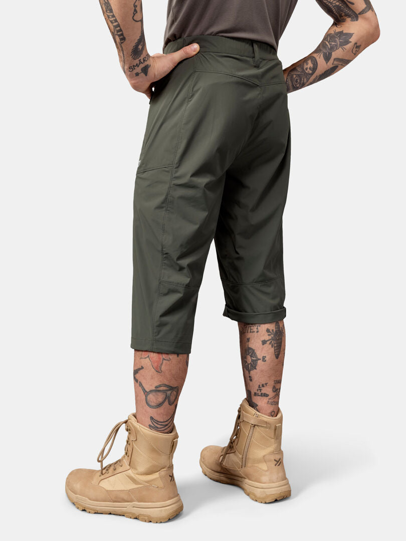 En person i Halti Pallas Cool X-stretch Capribyxor och solbruna stövlar, tatueringar på benen synliga, sedd bakifrån.