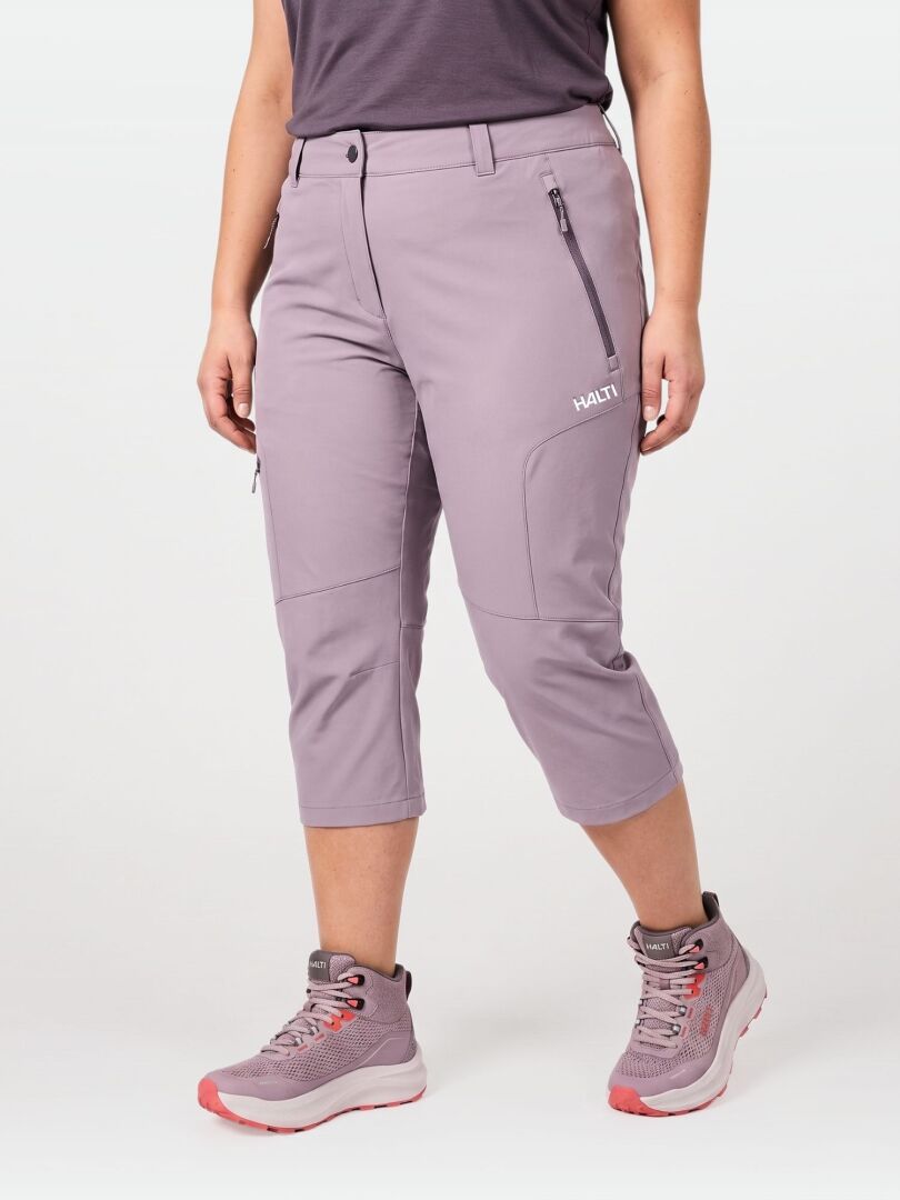 Person iklädd Halti Pallas Cool X-stretch Capribyxor Dam Plus, mörk topp och grå-rosa vandringsskor mot ljus bakgrund.