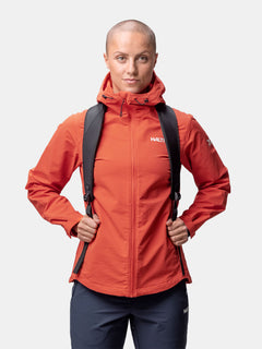 En person med rakat huvud bär en Halti Finholma X-stretch Jacka Dam och en svart ryggsäck mot en vit bakgrund.