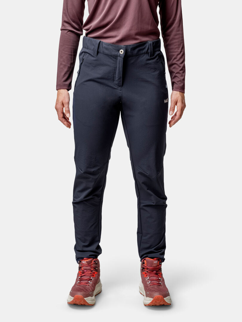 Person i långärmad rödbrun skjorta, Halti Finholma X-stretch Byxor Dam, och röda sneakers står mot en enfärgad bakgrund.