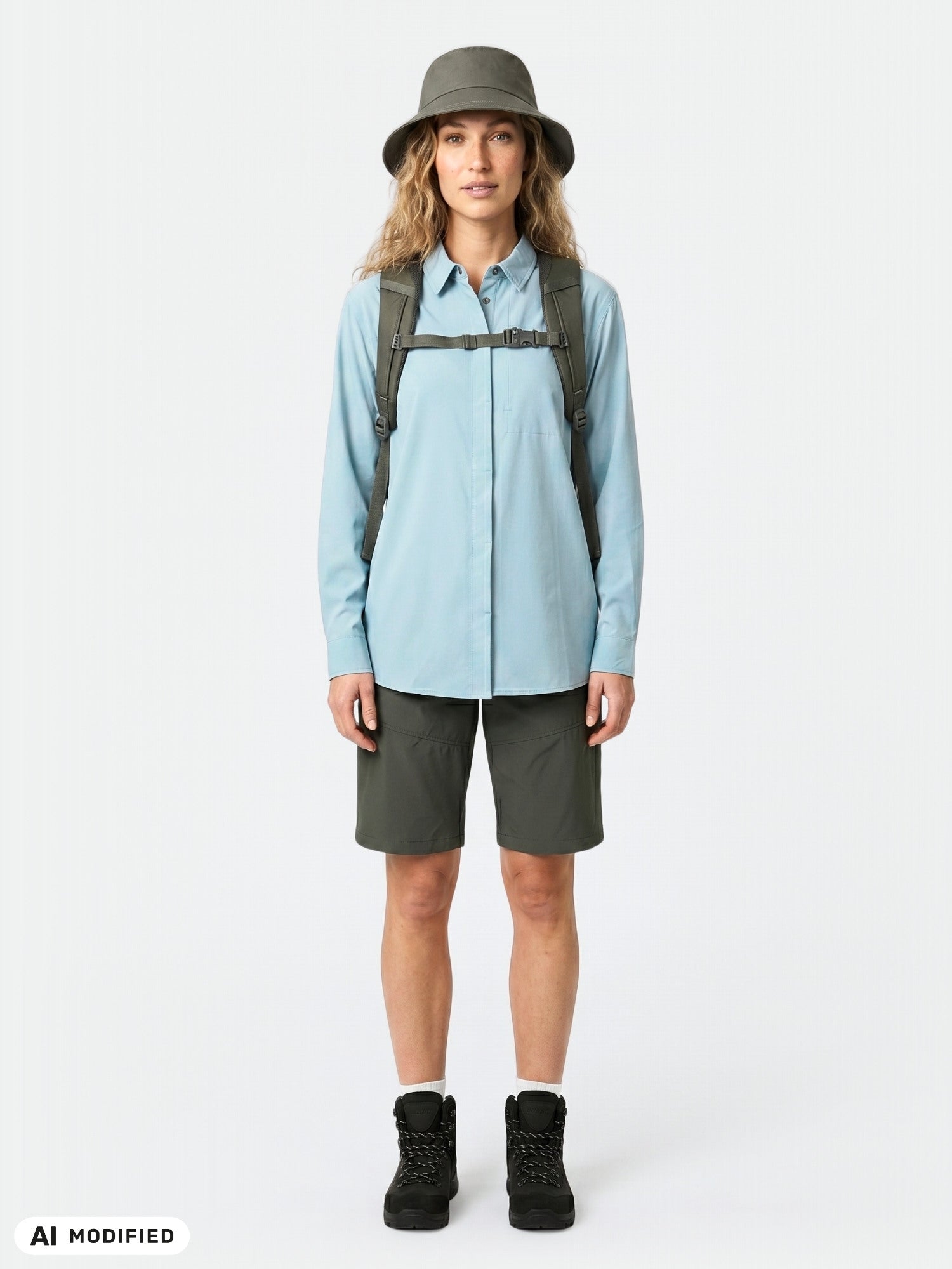 Person klädd i Halti Samoy långärmad funktionsskjorta för dam, mörka shorts, stövlar, mössa och ryggsäck mot vit bakgrund.