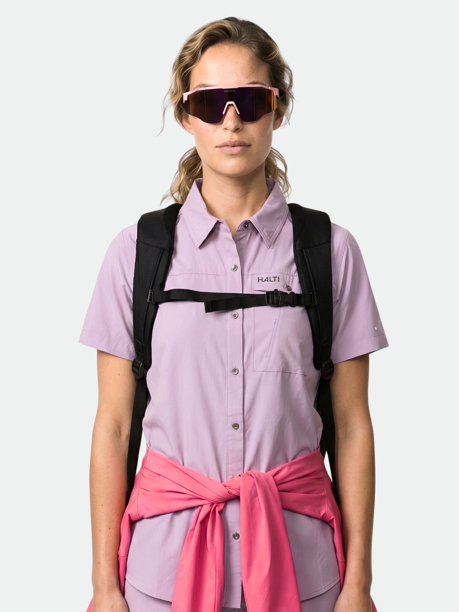 En person i Halti Samoy Funktionsskjorta Dam och solglasögon bär en svart ryggsäck med en rosa sweatshirt i midjan.