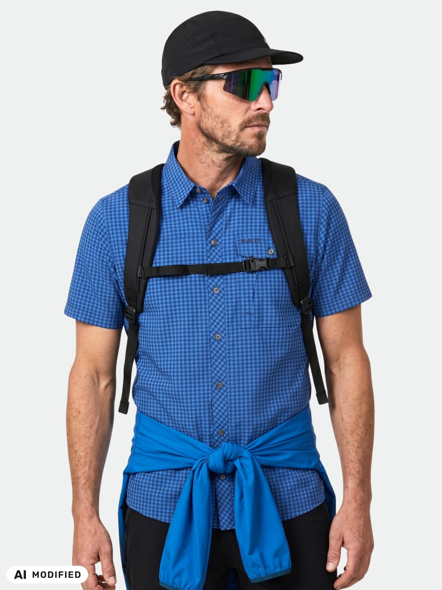 Man i Halti Samoy Funktionsskjorta, solglasögon, svart keps, snabbtorkande t-shirt, ryggsäck; sidovy.