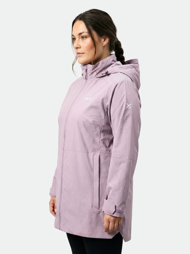 Kvinna i ljuslila Halti Valaja DX Parka Dam Plus står lite till vänster mot en enfärgad bakgrund.