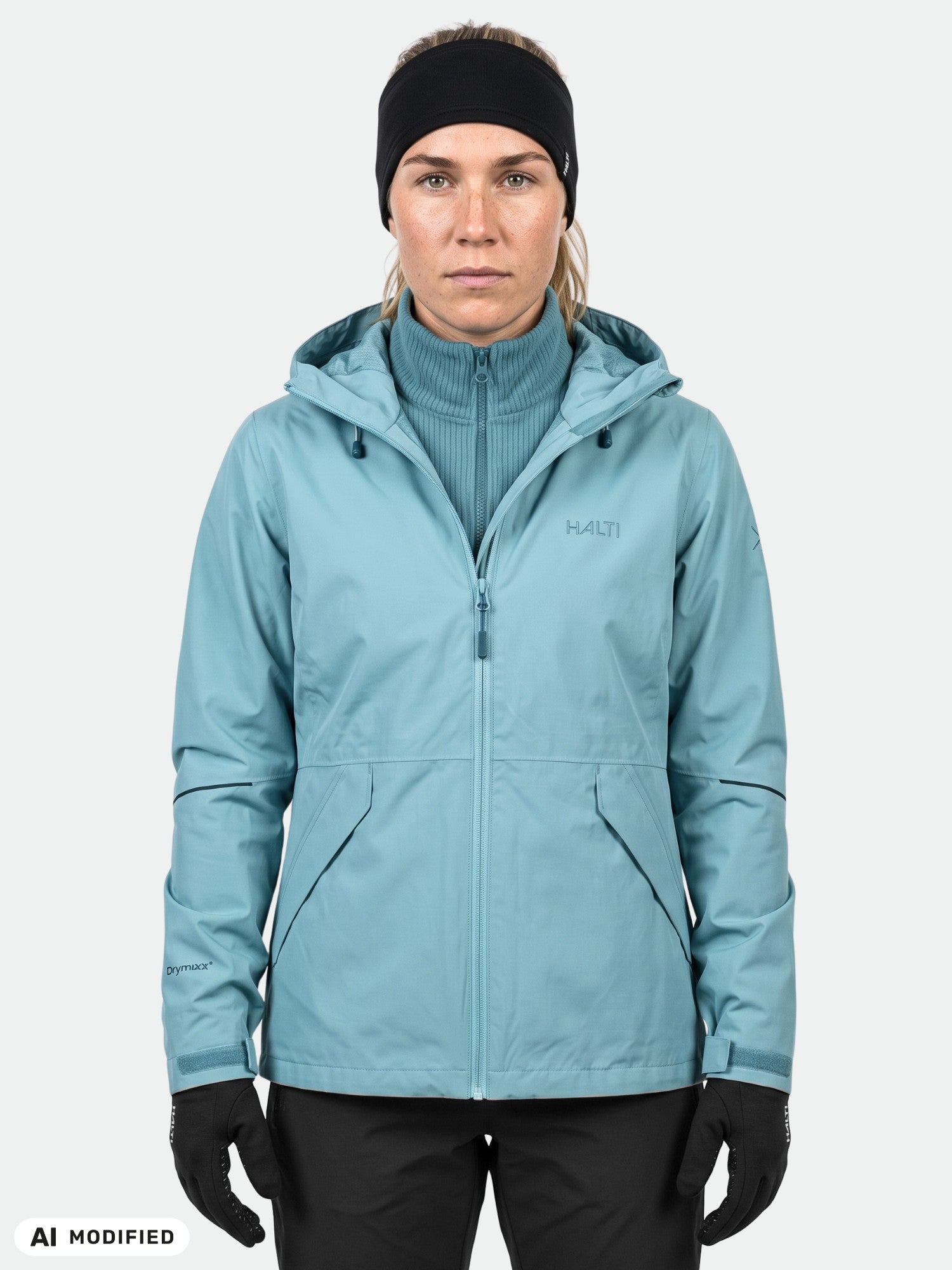 Modell klädd i Halti Loito 3-i-1 DX-jacka för damer, svarta handskar och pannband, stående mot en enfärgad bakgrund.