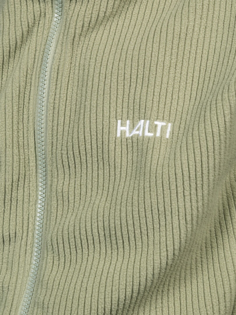 Närbild på en ribbad, ljusgrön Halti Loito 3-i-1 DX-jacka för dam med ”HALTI” broderat i vitt på bröstet.