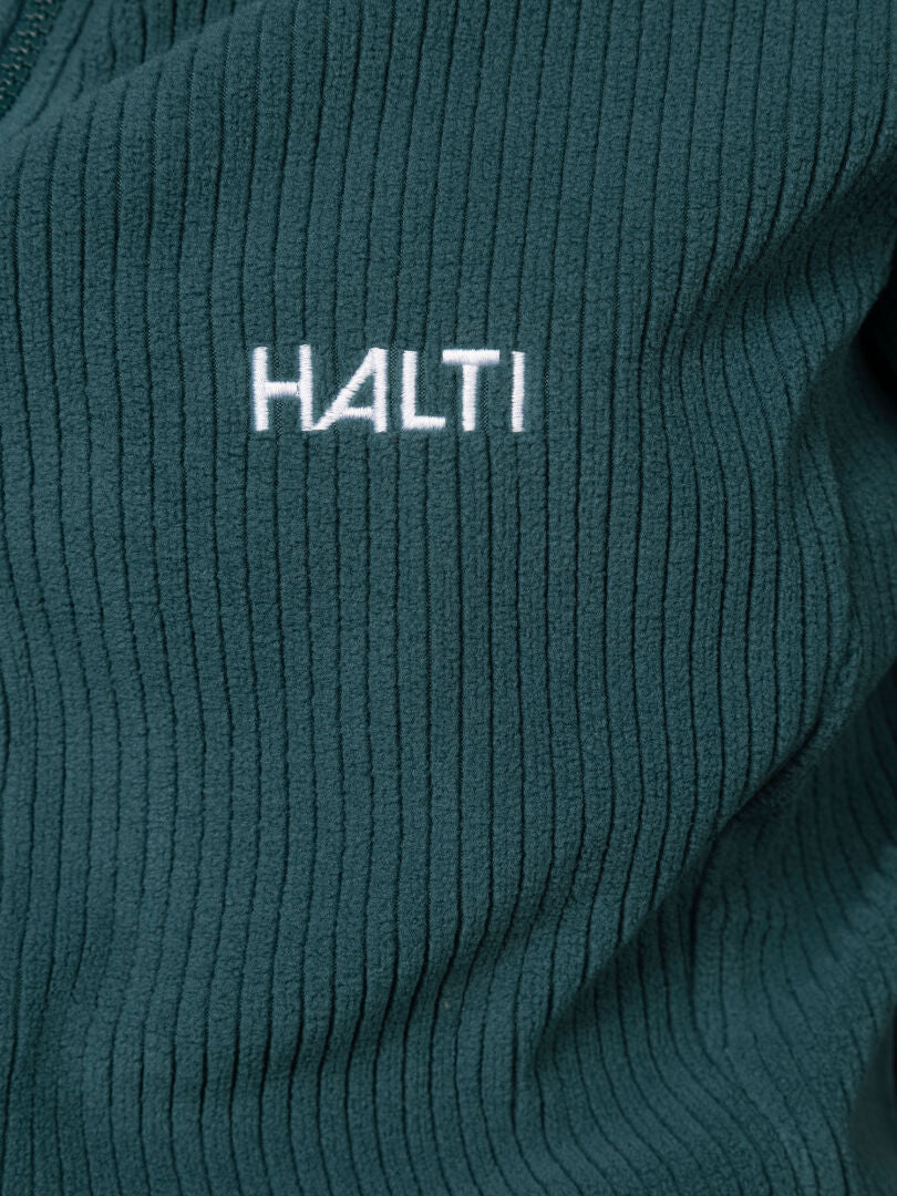 Närbild på det gröna, räfflade tyget på Loito 3-i-1 DX Jacka Dam med ”Halti” broderat i vit tråd.