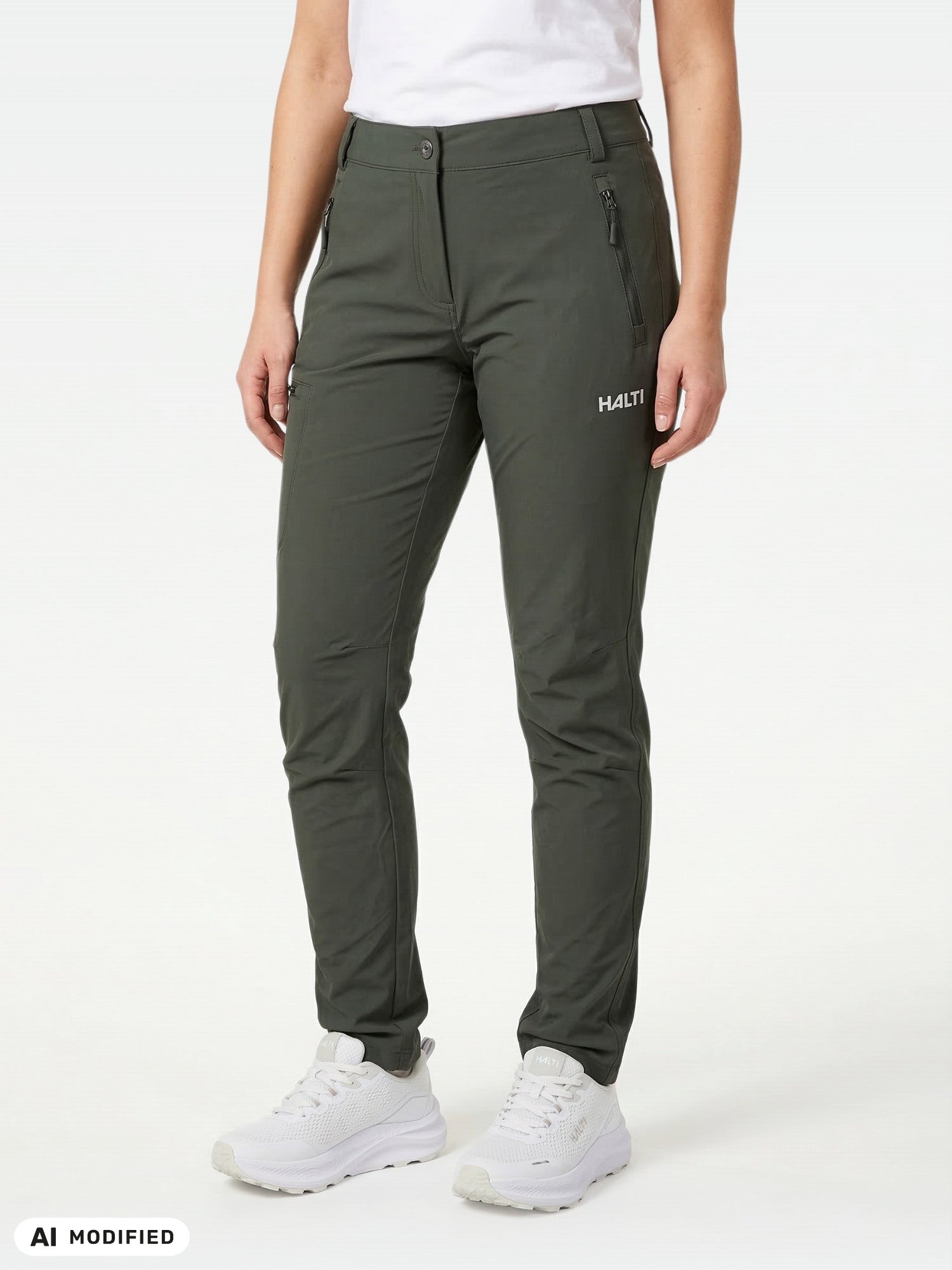 En person klädd i Halti Pallas X-stretch Outdoor Byxor Dam, en vit t-shirt och vita sneakers framför en enfärgad bakgrund.