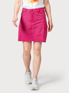 En person bär en ljusrosa Halti Reissu Dam Stretch Kjol, vit grafisk T-shirt och vita sneakers mot en enfärgad bakgrund.