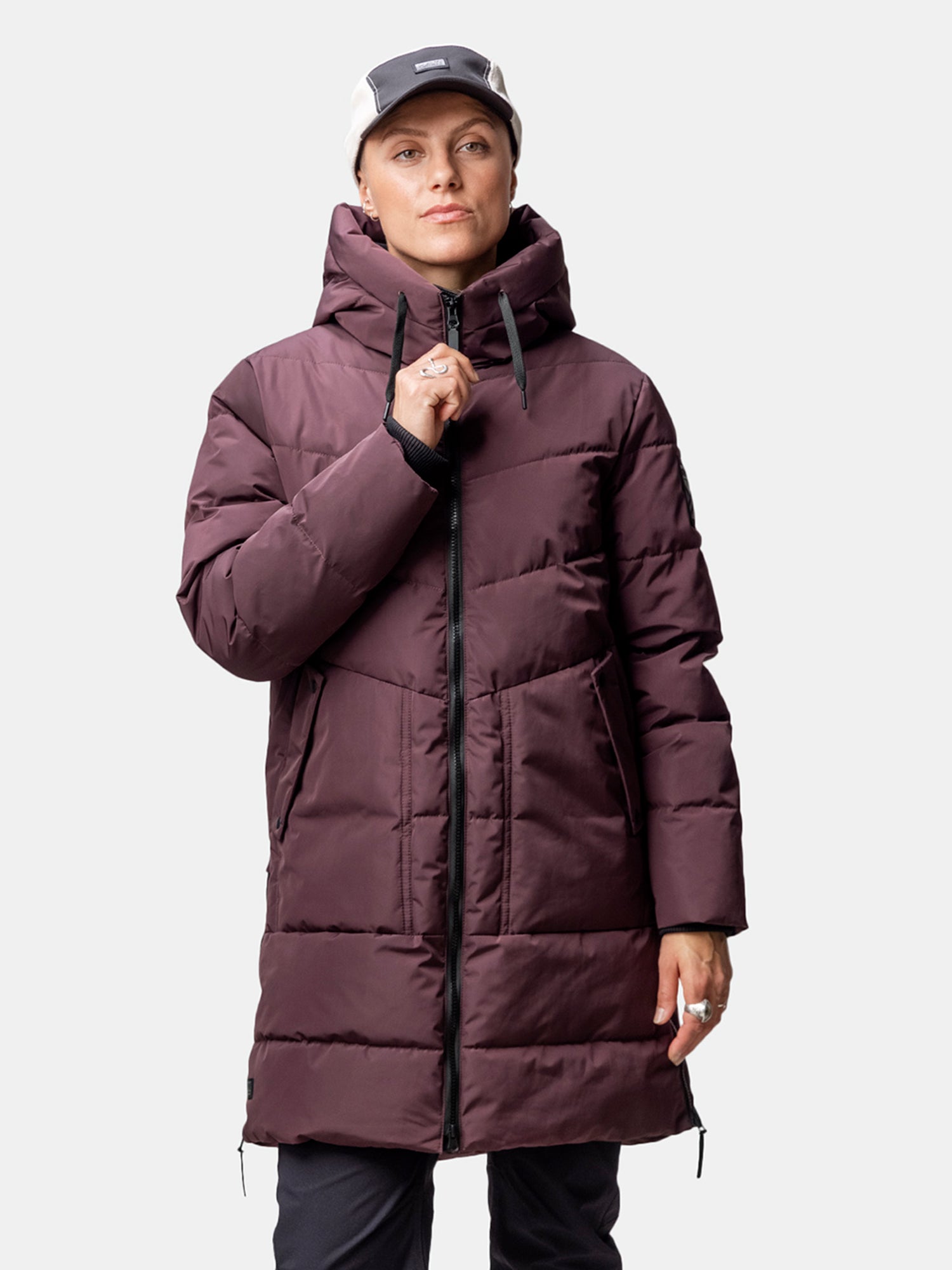 Personen bär Halti Linjat Parka Jacka Dam, svarta byxor och en ljus mössa mot en enfärgad bakgrund.