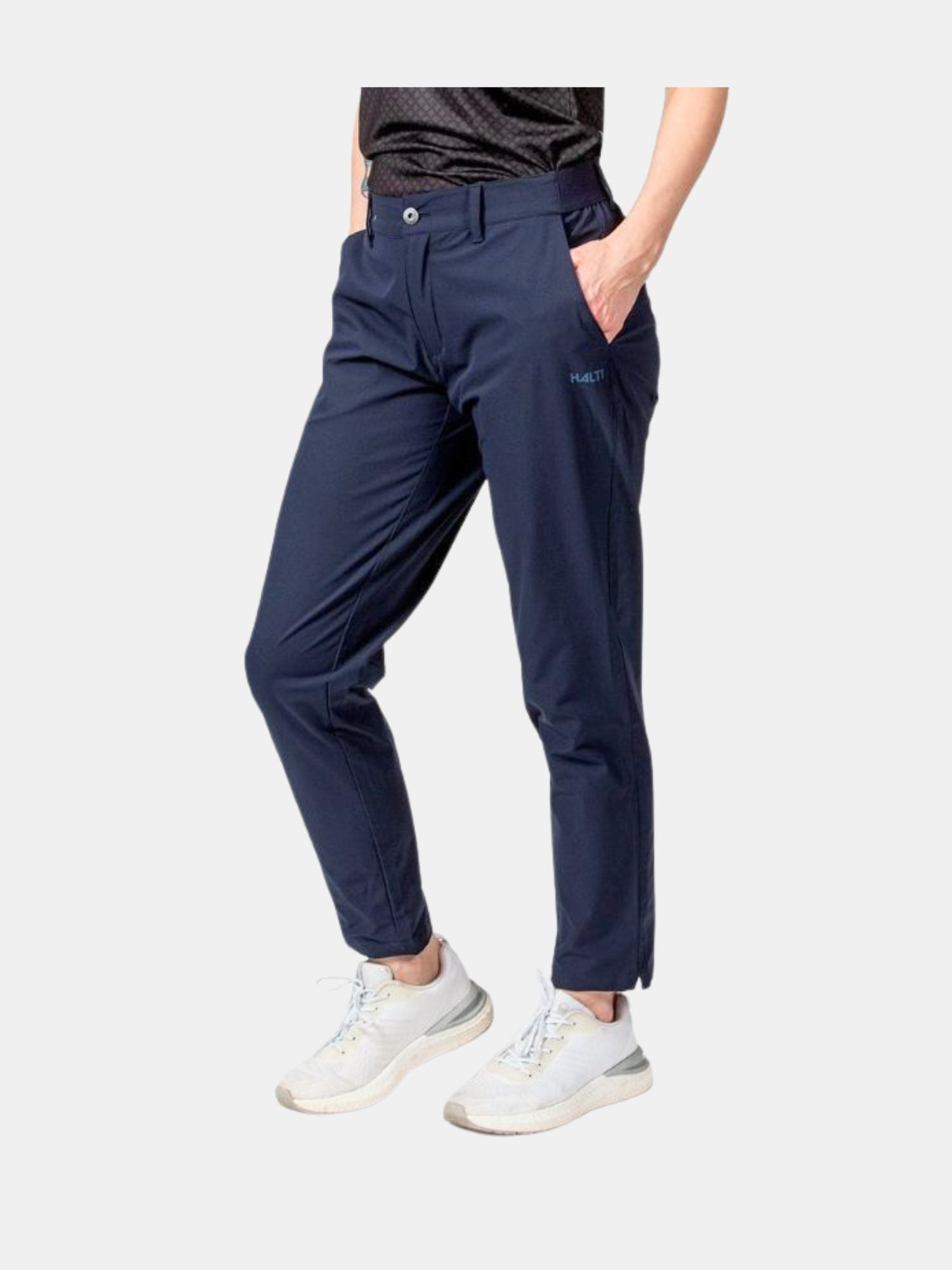Personen bär Halti Drive X-stretch Chinos Dam i marinblå färg, en svart skjorta och vita sneakers med händerna i fickorna.