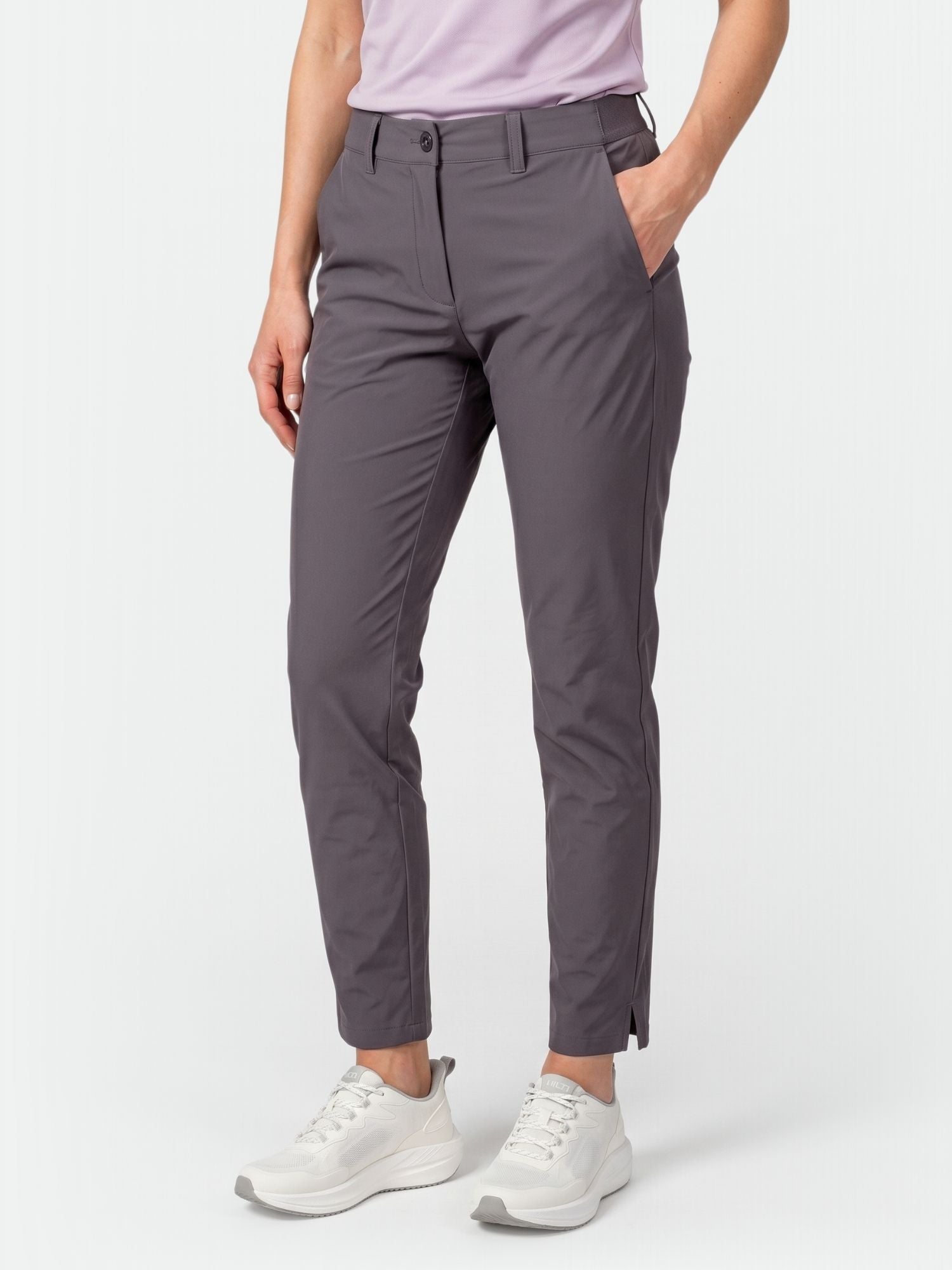 Kvinna klädd i Halti Drive X-stretch Chinos, vita sneakers och en ljuslila skjorta, handen i fickan.