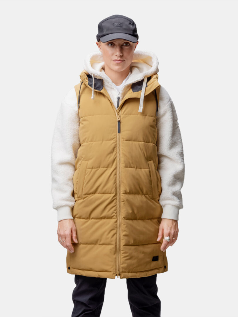 Kvinna i brun Halti Penger Puffer Väst Dam över vit huvtröja, svarta byxor och svart keps.