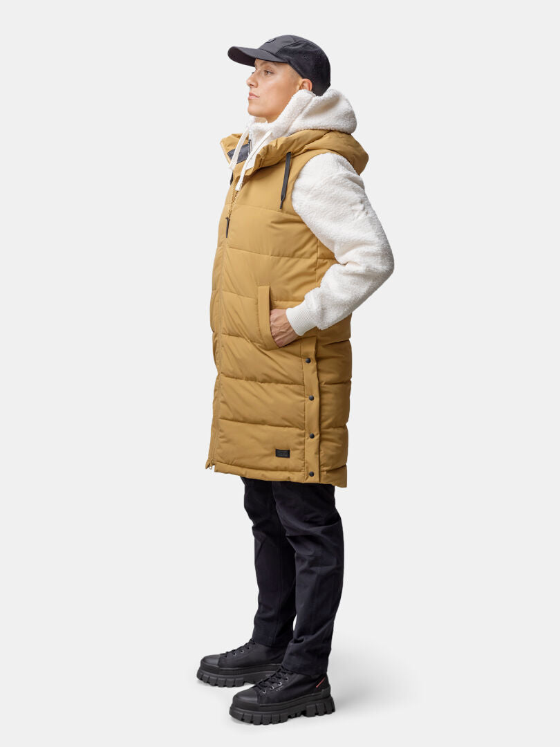 Person i Halti Penger Puffer Väst Dam, vit huvtröja, svarta byxor och keps, stående i profil.