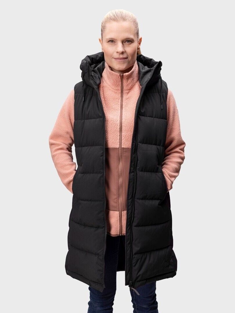 En kvinna bär Halti Penger Puffer Väst Dam i svart över en rosa zip-up, med händerna i fickorna, mot en enfärgad bakgrund.