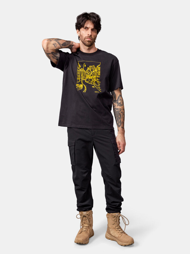 Man i Halti Skaltsi unisex t-shirt, svarta cargobyxor och solbruna stövlar med handen bakom nacken.